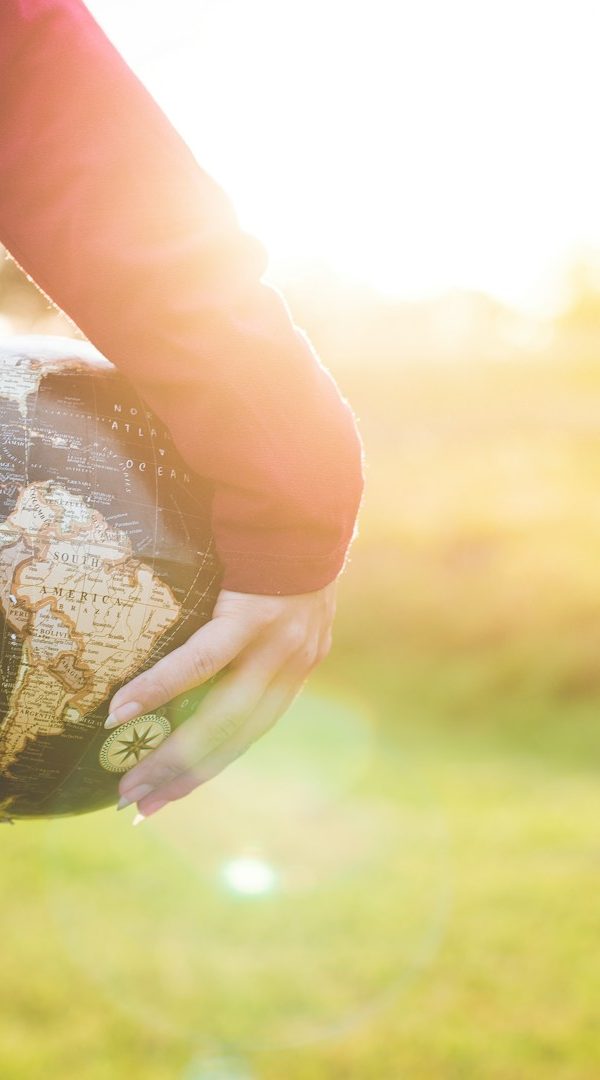 person holding black and brown globe ball while standing on grass land golden hour photography