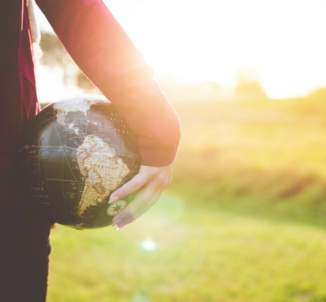 person holding black and brown globe ball while standing on grass land golden hour photography